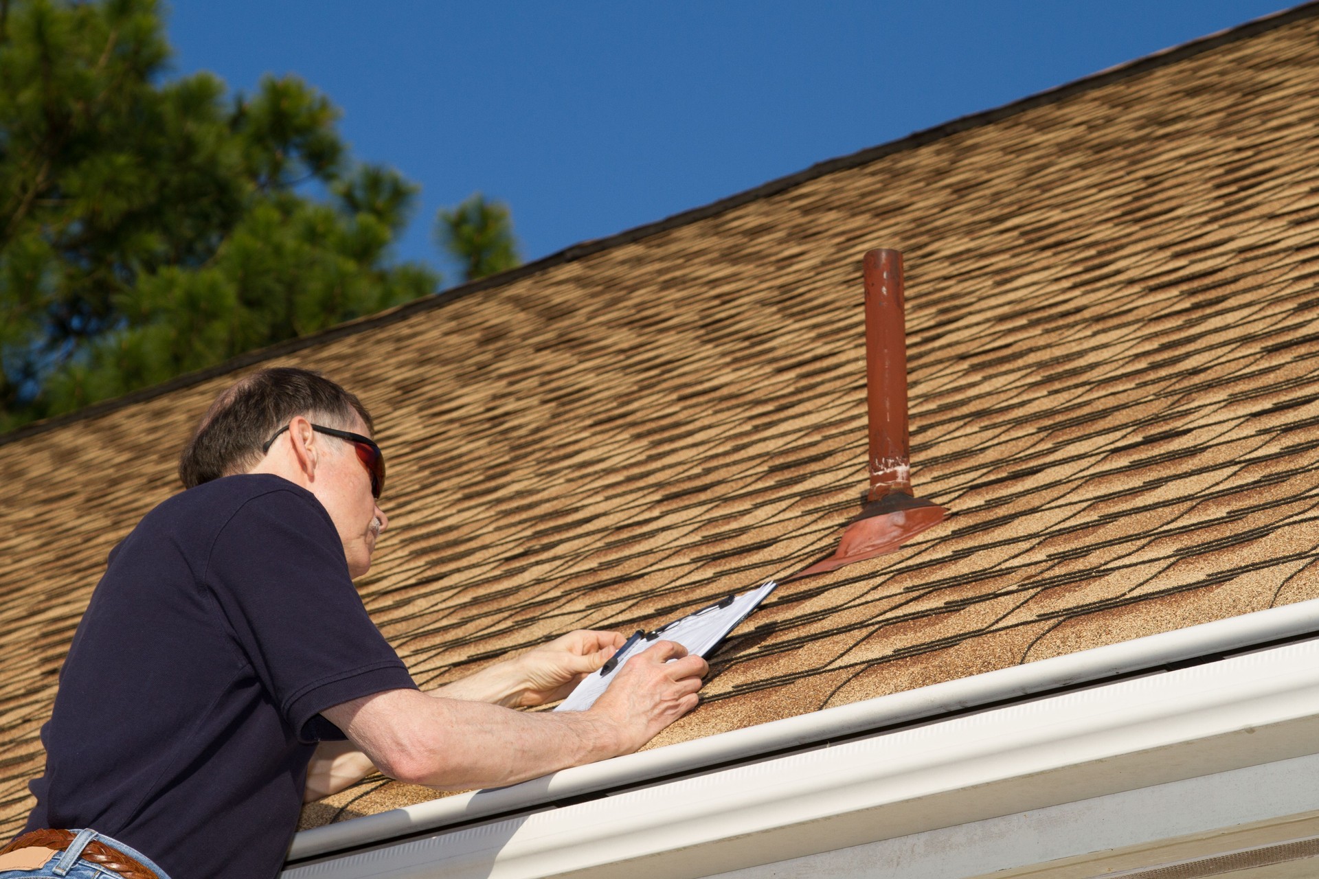 Home inspector reviews paperwork on a roof edge.